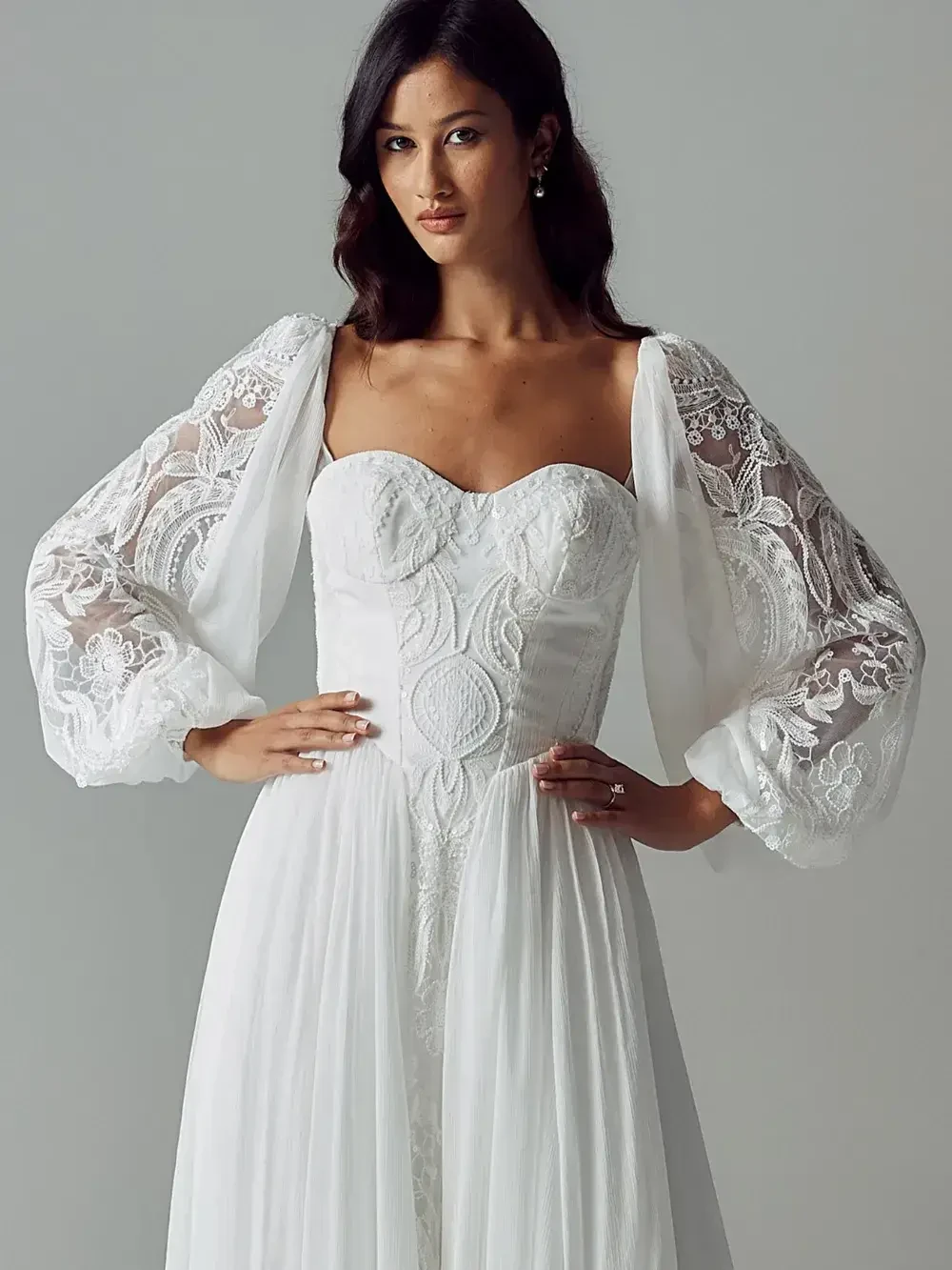 Woman in an elegant white wedding dress with lace sleeves and a sweetheart neckline, exuding sophistication and confidence.