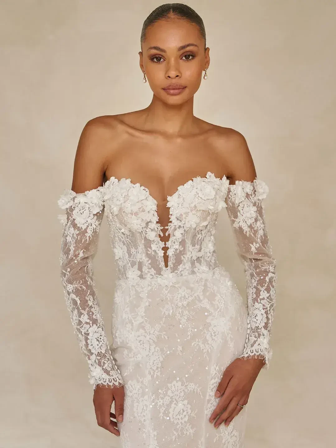 A woman wearing an elegant off-the-shoulder white wedding dress with intricate lace details and floral embellishments.